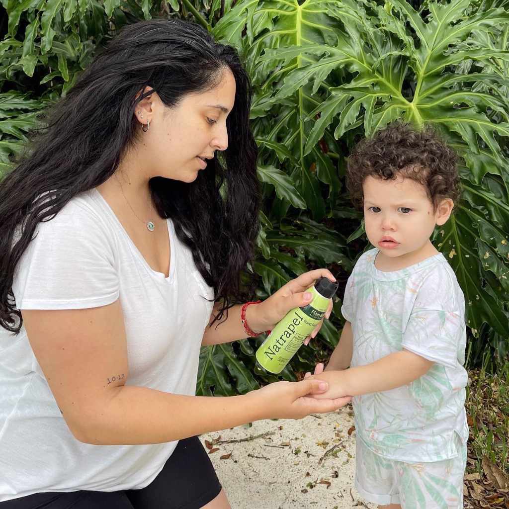Natrapel Lemon Eucalyptus Tick & Insect Repellent Eco-Spray 6 oz. mother spraying on child's arm in front of leafy trees