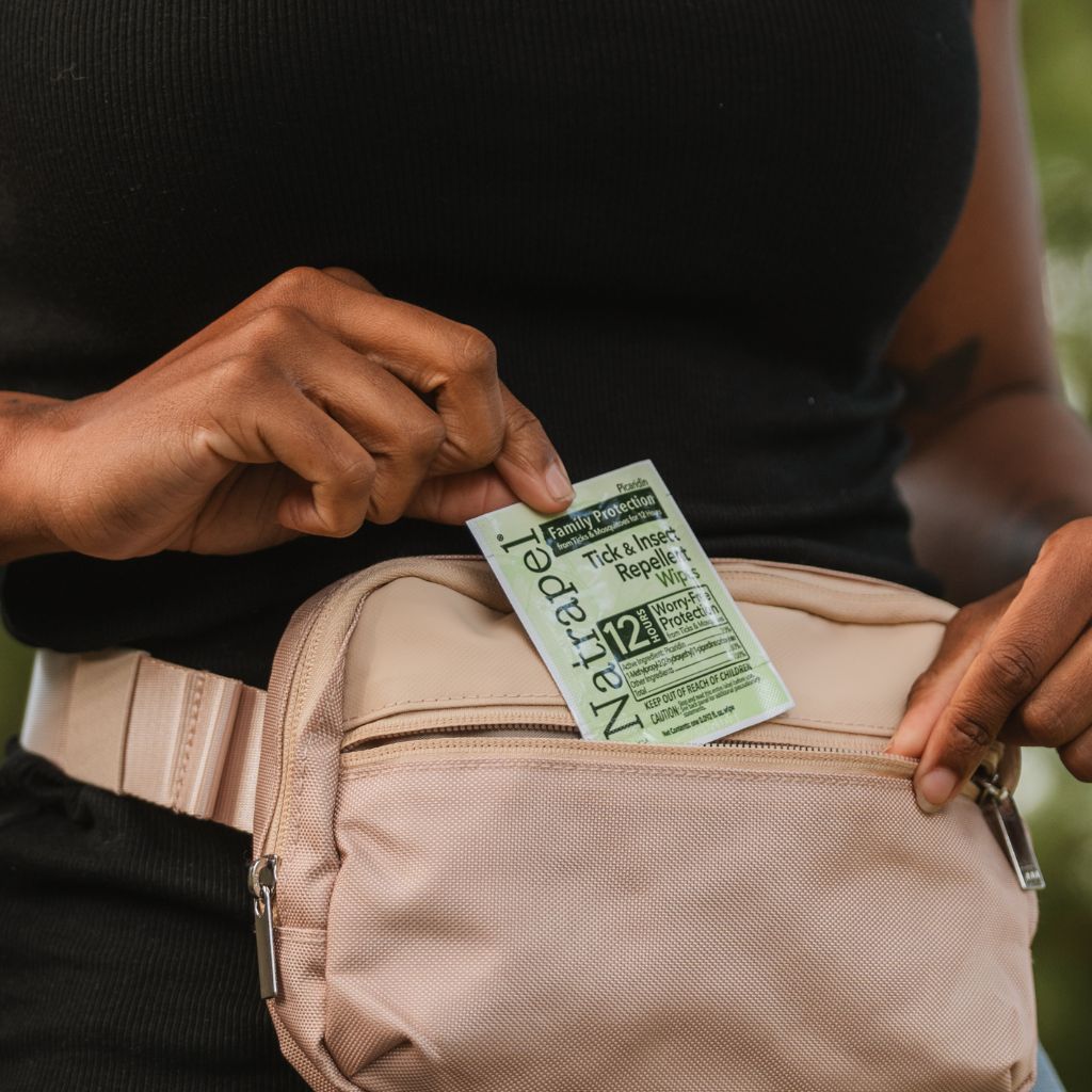 Person holding a Natrapel insect repellent packet over a beige bag.