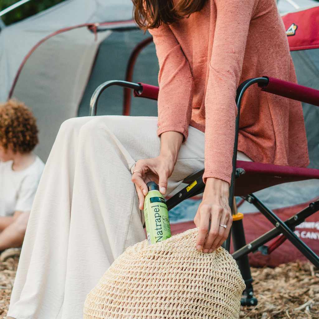 Natrapel Lemon Eucalyptus Tick & Insect Repellent Eco-Spray 6 oz. woman pulling from raffia handbag while sitting in a camp chair
