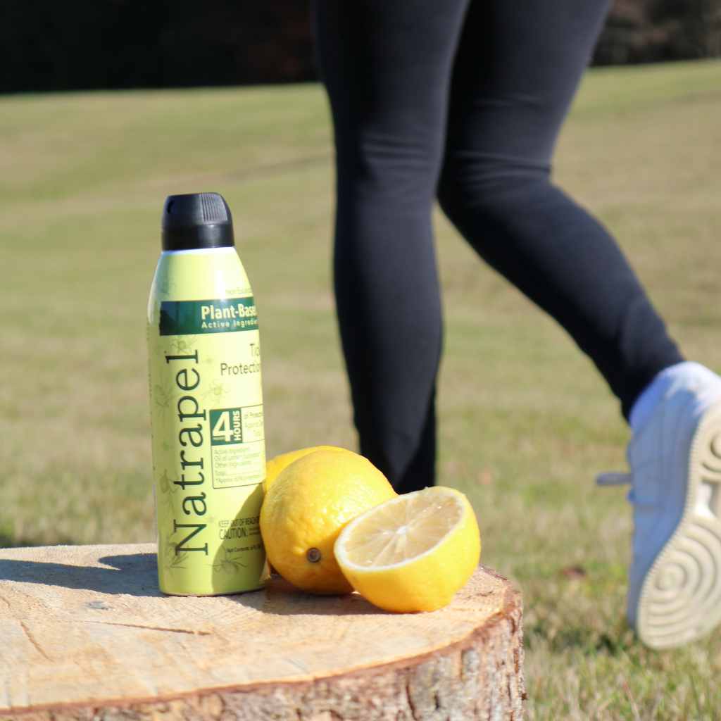 Natrapel Lemon Eucalyptus Tick Repellent Eco-Spray 6 oz. posed next to lemons on a stump with person walking behind