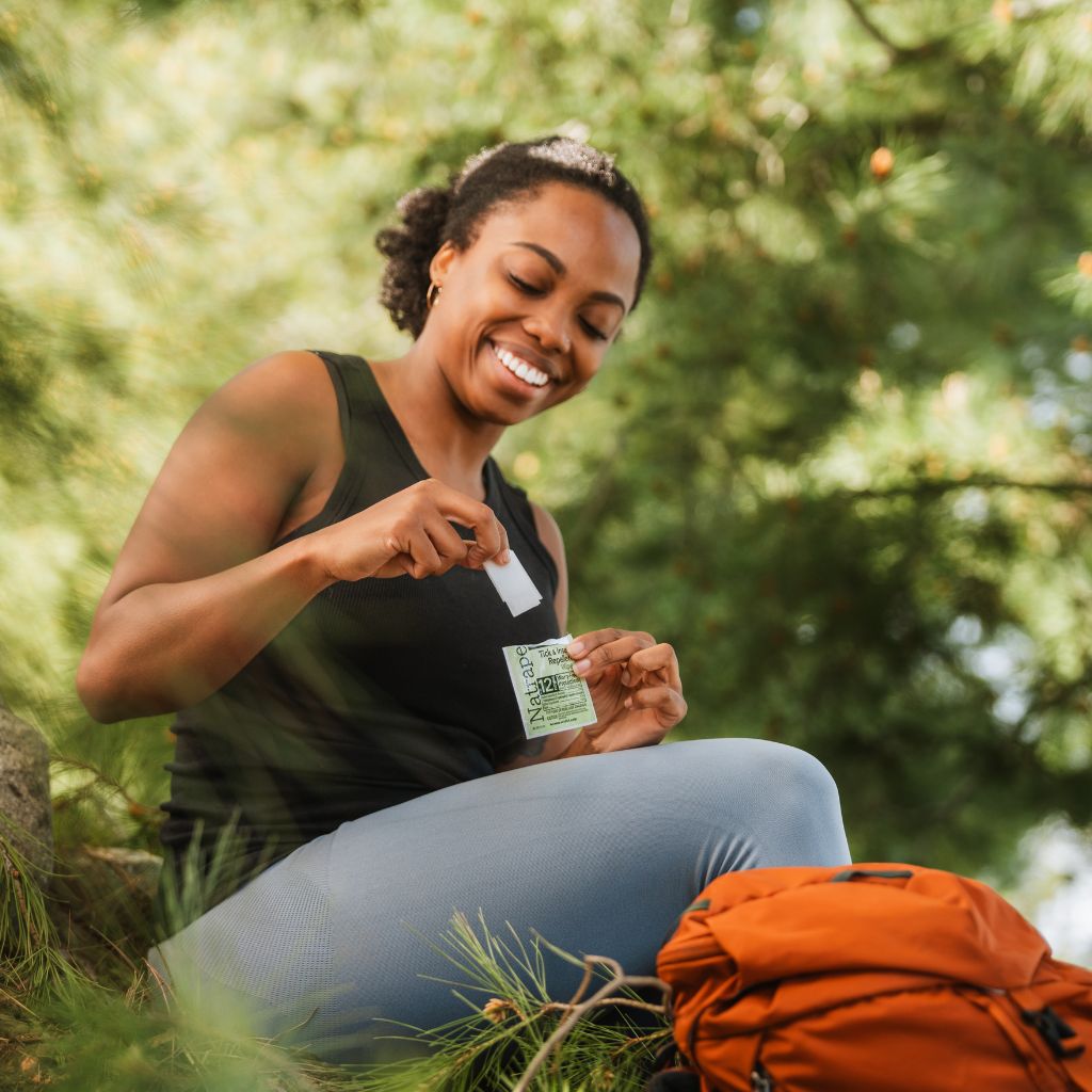 Woman sitting outdoors holding a Natrapel wipe with trees in the background