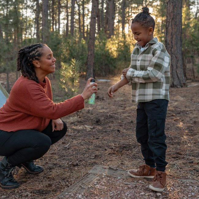 child being sprayed on arm with insect repellent by an adult