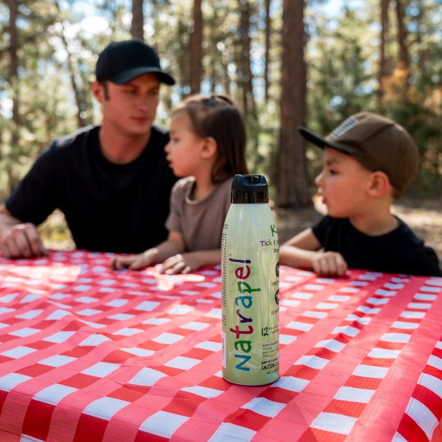 family sitting on a picnic table with a Natrapel Kids can in front of them 